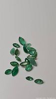 Photo shows 15 marquis cut natural Zambian emerald gemstones arranged on a plain surface, highlighting the green hue and faceted cuts.