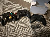 Three gaming controllers displayed: Nintendo GameCube wired controller, two black wireless Xbox Series X/S controllers with one USB cable
