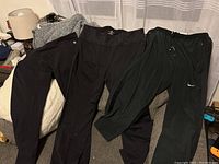 Five pairs of black athletic pants including visible Nike Dri-Fit pants with white swoosh logo, and Tuff Athletics pants show small logo by waistband.