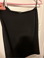 Black pencil skirt made from smooth black fabric hanging on hanger, the fabric appears lightweight and formal.