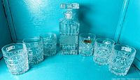 Full set showing the decanter surrounded by six whiskey glasses on a blue background