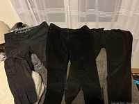 Three pairs of Calvin Klein black pants laid out: two corduroy and one cargo capri style.