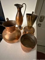 Four copper decorative items are arranged on a light surface showing color and patina variations.