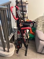 Side angle showing full bike frame with red padded handles, arm resistance bands, and pedal area