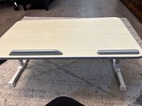 Front view of light-colored laptop desk surface with two rubber stoppers and white legs folded out, placed on carpet.