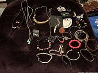 Wide view of all costume jewelry items arranged on dark fabric including necklaces, bracelets, earrings, and a few boxed pieces.