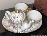 Miniature porcelain tea set including teapot with lid, two cups, and two saucers showing floral pattern and gilded gold accents.