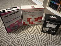Three boxed party games displayed on a patterned rug: Think Like The Herd, An Outrageous Party in a Box, Bad People.