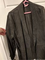 Front and part of sleeve detail of the dark suede jacket on a hanger.