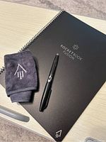 Front cover of Rocketbook Fusion notebook with pen and cleaning cloth on a light wood surface.