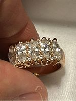 Close-up of gold-toned ring held by fingers showing seven clear marquise-cut stones in prong settings on the band.