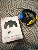 Controller grip packaging and wired headset lying next to it on fabric.