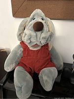 Front view of vintage Ganz Wrinkles plush dog puppet seated, showing detailed face, blue eyes, big brown nose, and wearing red corduroy overalls with white shirt underneath.