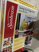 Photo showing Sunbeam boxed Swing Out Fridge Shelf with branding and depiction of product in use on fridge shelf holding chilled items.