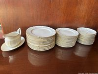 A full view of the Noritake Chandon ivory dinnerware plates stacked in three different piles and the creamer with saucer on the side, showing the full set arrangement.