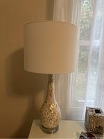 Side view of one lamp positioned near window; shows overall lamp shape, white lampshade, and base mosaic pattern with pearl pieces embedded in acrylic.