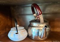Two teapots side by side on a wooden surface showcasing the front and top view, highlighting the materials and handle shapes.