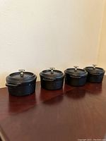 Front angled view of four mini cast iron Dutch ovens in a row showing lids with silver knobs and rounded handles