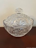 Close-up image of clear crystal cut glass candy dish showing intricate floral and geometric patterns with faceted knob on lid.