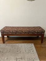 Front view of rectangular bench showing floral cushion and wooden legs.