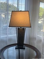 Front angle view of the lamp showing trapezoid base with inset textured panel and fabric shade.