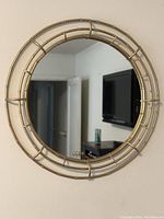 Photo of a round wall mirror with a gold metal bamboo-style frame and clear reflective surface.