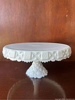 Front side view of milk glass cake platter showing decorative edge and pedestal base.