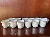 Front view showing 13 ivory Noritake Chandon tea cups with decorative embossed pattern and gold trim on rim and handles.