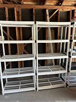 Front view of three white plastic shelving units with four shelves each, placed side by side in a garage or storage area.