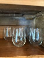 Photo showing three of the five clear stemless wine glasses arranged in a row on a wooden surface.