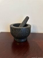 Dark gray granite mortar with pestle inside on wooden table.