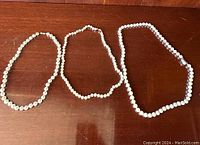 Three vintage faux pearl necklaces laid out on a wooden surface, showing overall condition and bead sizes.