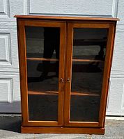 Front view of vintage walnut bookcase with closed glass doors showing wood grain and brass handles.