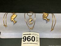 Overview of six gold jewelry pieces displayed on gray cushion