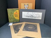 Full collection photo showing two folio prints, signed book, ink drawing, and cat print in mats