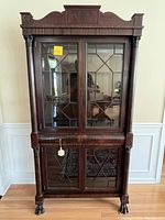 Front view of antique china cabinet with closed glass doors, claw feet visible, wooden crown molding top