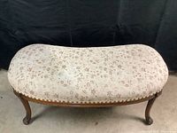 Front view of kidney-shaped bench showing the floral upholstered seat and wood frame with cabriole legs.