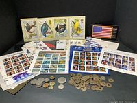 Group of coins and multiple uncut stamp sheets arranged on black background