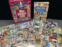 Two hardcover baseball card reference books with a spread of loose Topps cards on black background