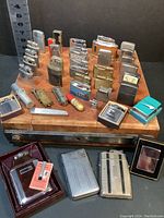 Overview of lot: approx. 28 flip-top lighters arranged on wood block with 3 cases in front
