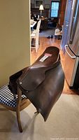 Side view of the Borelli English saddle on a chair, showing smooth brown leather seat and flaps with textured darker panels