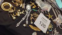 Photo showing mixed broken jewelry items including pearl drop earrings, rhinestone dangles, gold-tone hoop earrings with heart, cameo pin, filigree earrings, necklace extenders, watch parts, and a MaxSold tag.