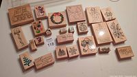 All 24 wooden rubber stamps with Christmas holiday designs shown laid out on white surface.