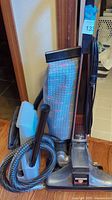 Full view of Kirby Heritage II vacuum with hose and attachments in front of doorway on hardwood floor.