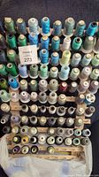 Full view of wooden thread rack filled with spools of thread. Threads predominantly blues, greens, and neutrals, many still wrapped.