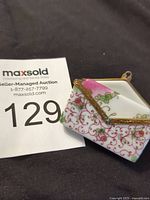 Porcelain envelope-shaped box with detailed floral and gold designs next to auction number