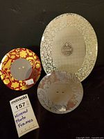 Photo showing all three mirrored glass photo frames arranged on a surface including the large oval and two smaller round frames, one red and one silver bordered.