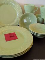 Full view of four celery green dinner plates, four bowls, and four mugs featuring fruit and leaf embossed design
