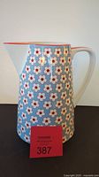 Full view of porcelain pitcher showing light blue body with repeated white and red floral motif and spout and handle shape.