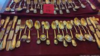 Top-down view of the full flatware set arranged on a maroon fabric tray inside a tarnish-proof roll, showing multiple rows of knives, forks, spoons, and serving utensils.